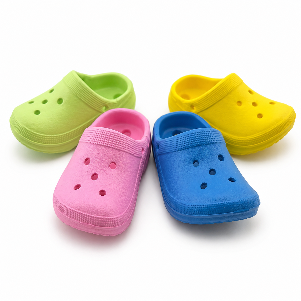 Four colorful plastic clogs in green, pink, blue, yellow on white background