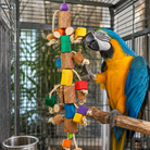 Blue-and-yellow macaw playing with colorful wooden block bird toy on rope inside cage